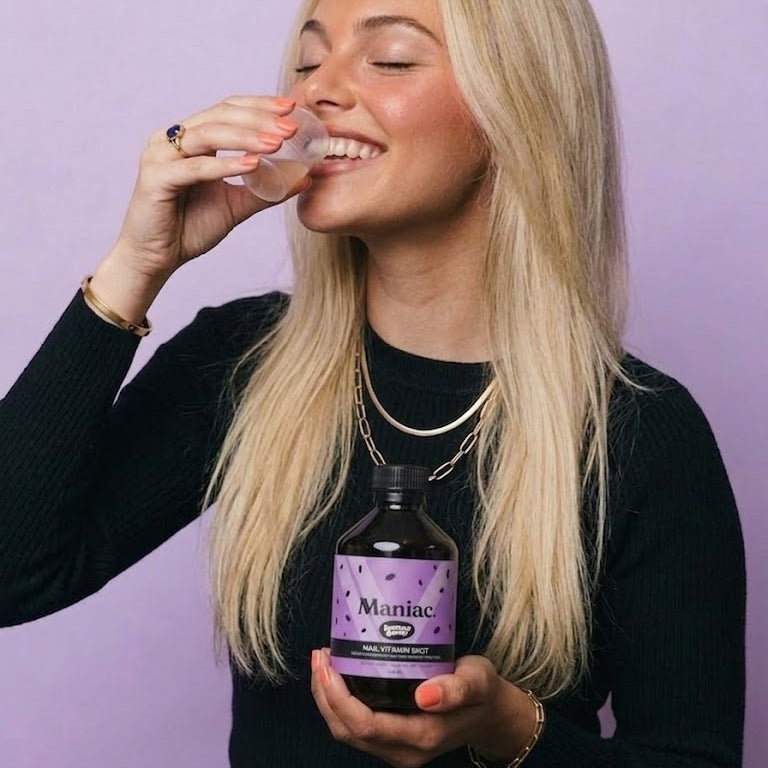 Lifestyle: woman taking her daily 20 ml Nail Vitamin Shot, alongside the Maniac Nails bottle.