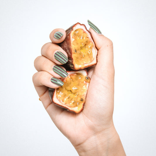 Hand with Stripe Tease gel nail stickers by Maniac Nails holding passion fruit, green pinstripe nails