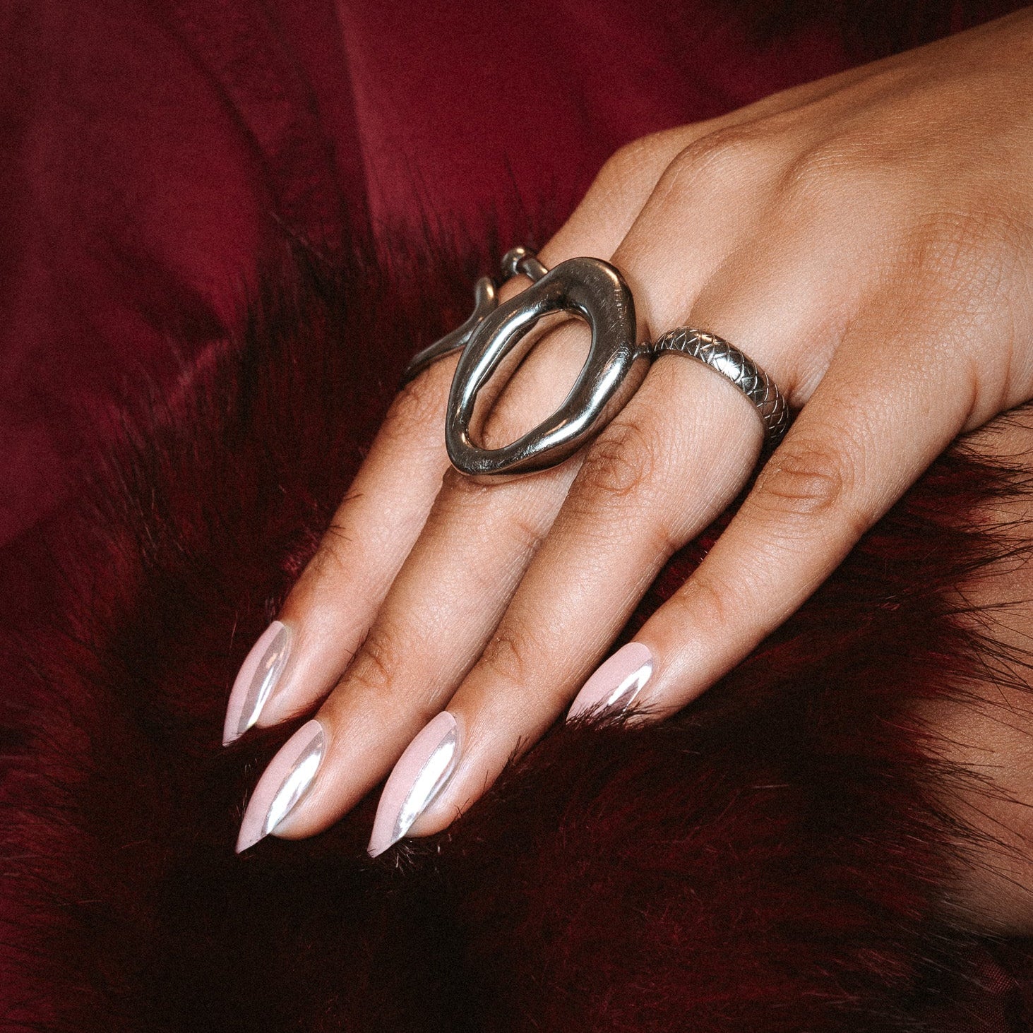 Vedder & Vedder silver strike Maniac Nails light pink with silver line side of nail on hand with silver rings and dark red fur