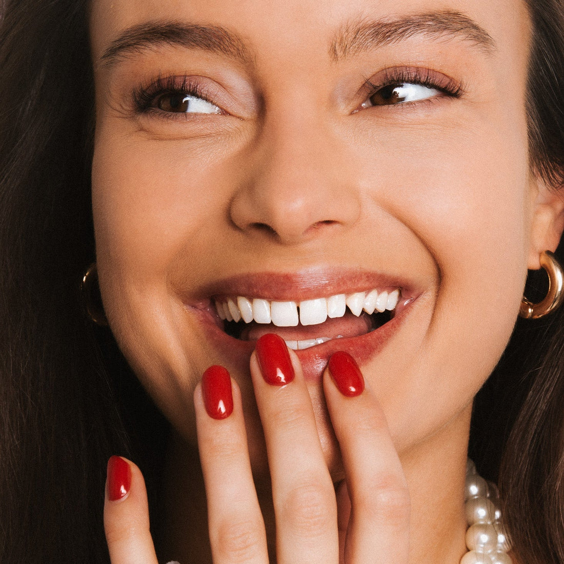 Smiling woman with red gel nails and pearl necklace