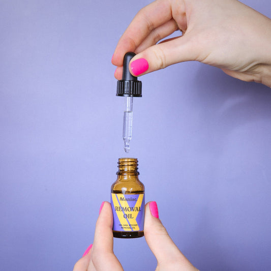 Hands with bright pink nails holding a Maniac Removal Oil dropper bottle