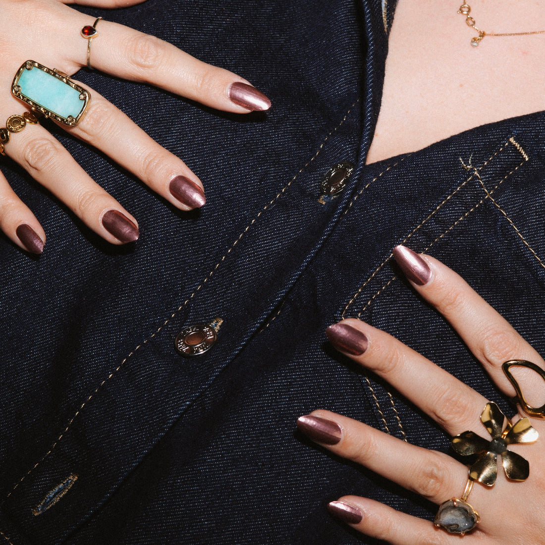 Woman's hands with chrome mauve gel nails on denim jacket with gold rings