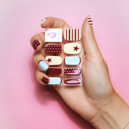 Hand holding All In gel nail sticker sheets by Maniac Nails on a pink background