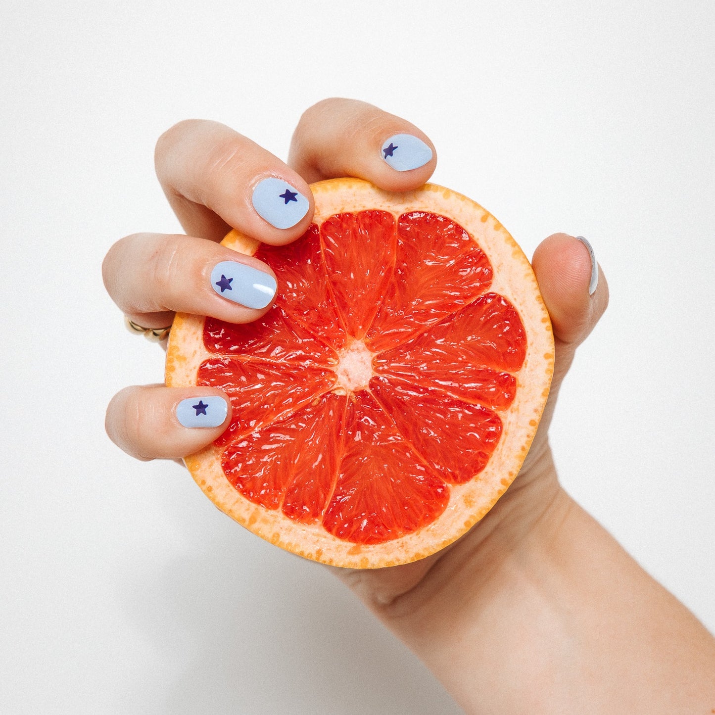 Hand with Blue Wish gel nail stickers by Maniac Nails holding a grapefruit, light blue nails with navy star