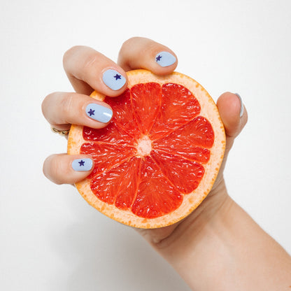 Hand with Blue Wish gel nail stickers by Maniac Nails holding grapefruit, light blue nails with navy stars