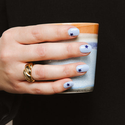 Hand with Blue Wish gel nail stickers by Maniac Nails holding a cup, light blue starry nails