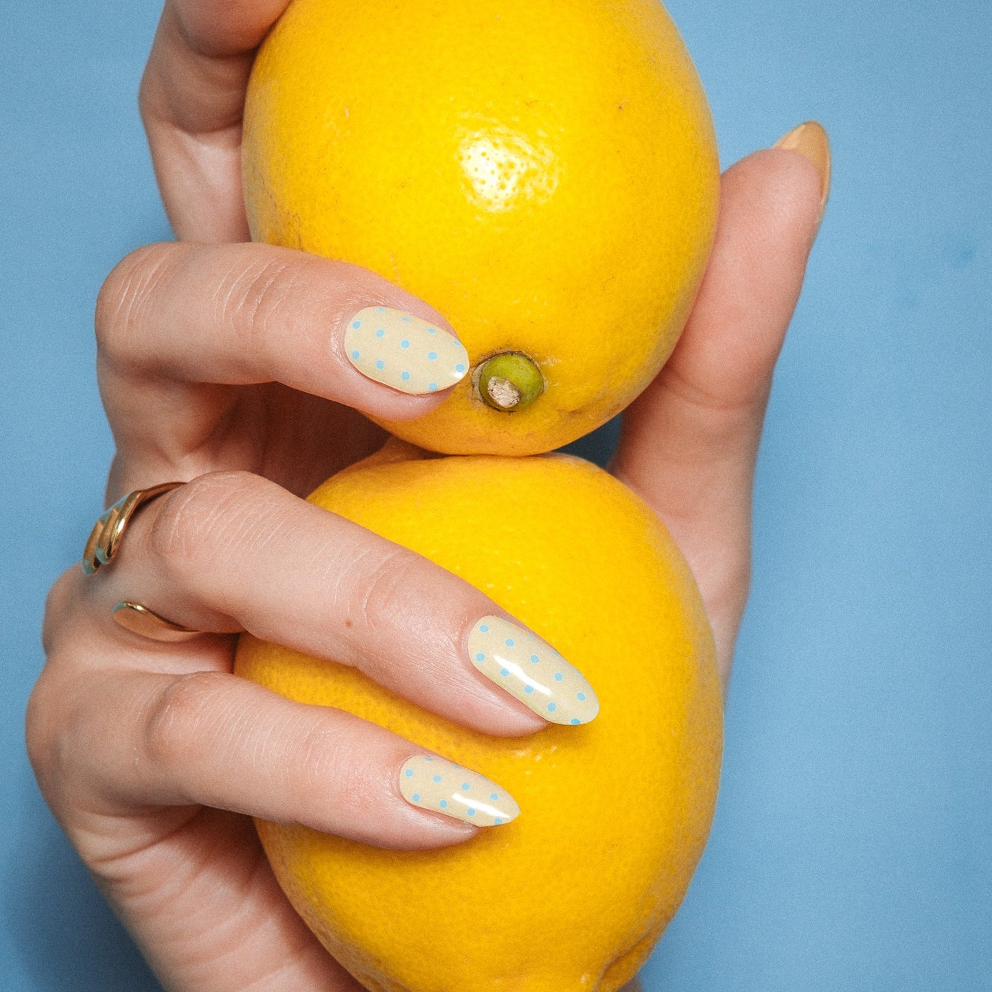 Hand with Butter Dots gel nail stickers by Maniac Nails holding lemons, butter yellow nails with little dots