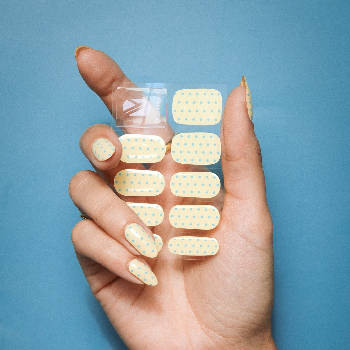 Hand holding Butter Dots gel nail sticker sheet by Maniac Nails, butter yellow nails with dots