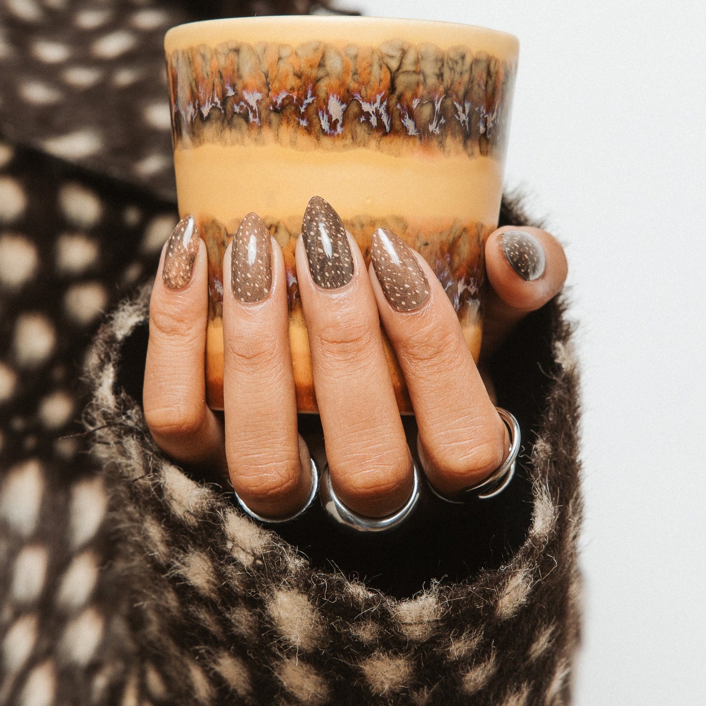 Hand with Deer Me gel nail stickers by Maniac Nails holding a cup, fawn speckled manicure