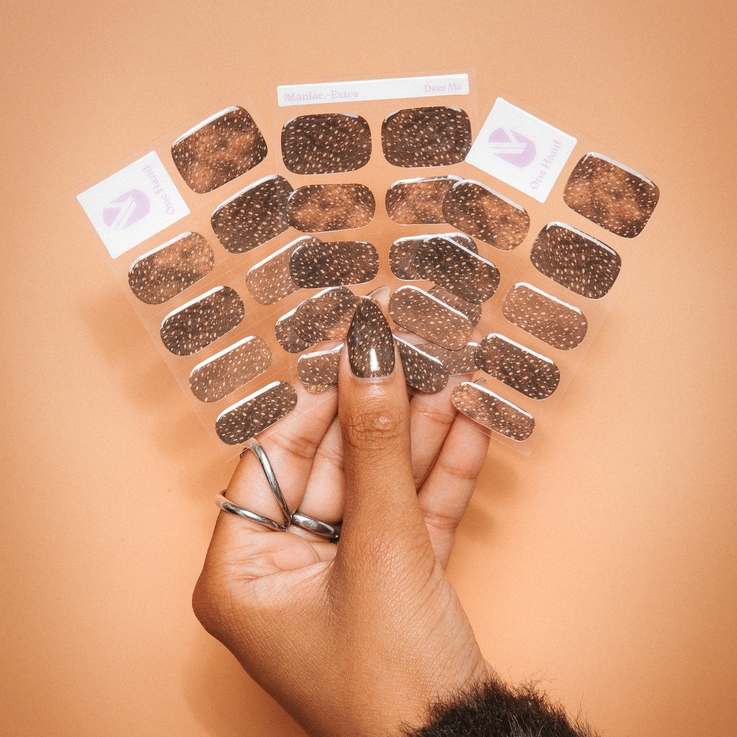 Hands holding Deer Me gel nail sticker sheets by Maniac Nails, brown speckled nail wraps