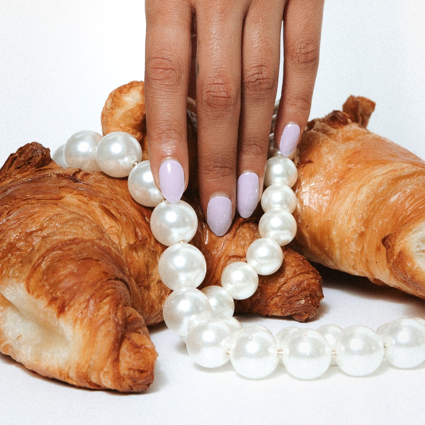 Giselle Gray Maniac Nails grey nail design sticker on hand with croissant and pearl necklace 