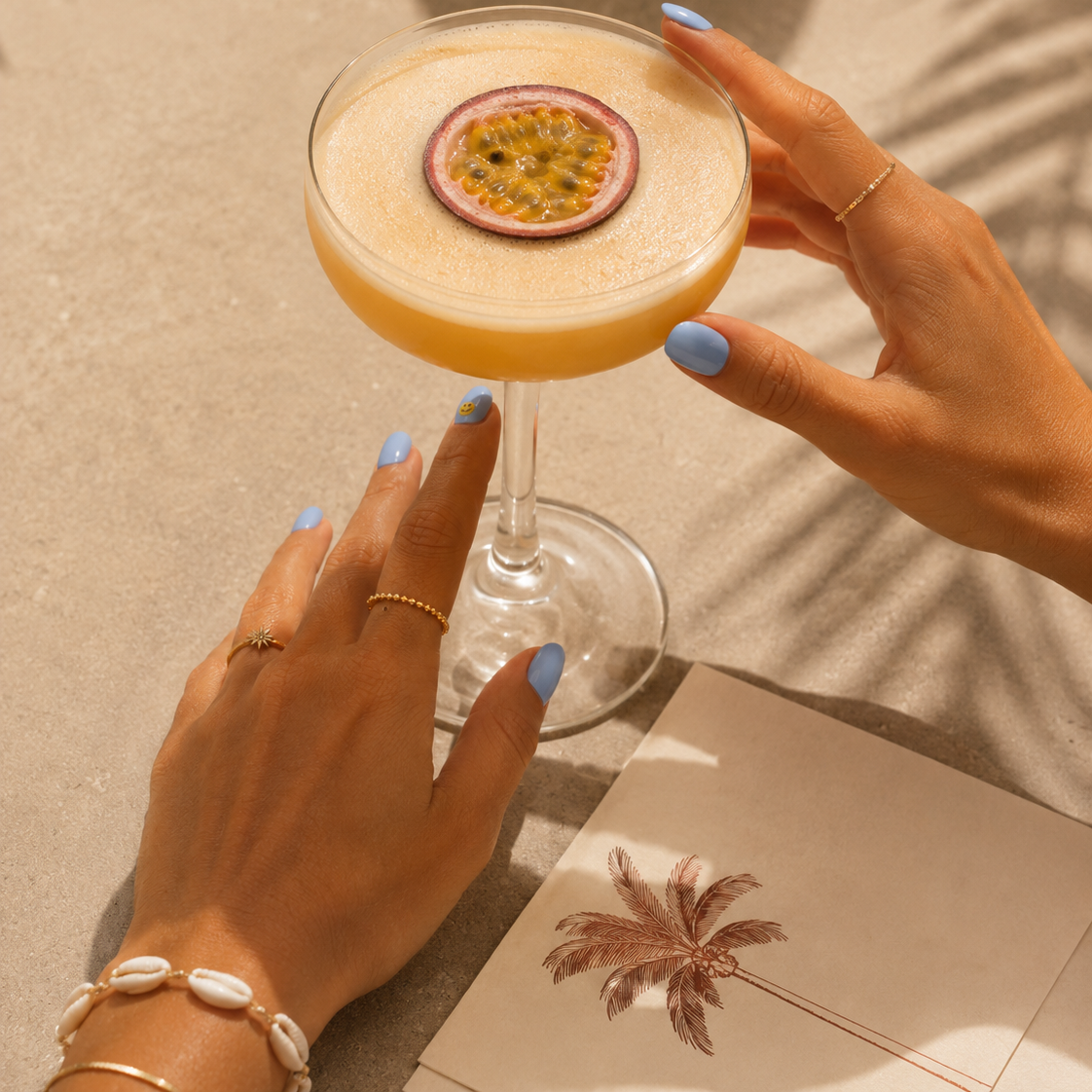 Good Vibes Only sky blue gel nail stickers by Maniac Nails, holding a passion fruit cocktail in sunlight