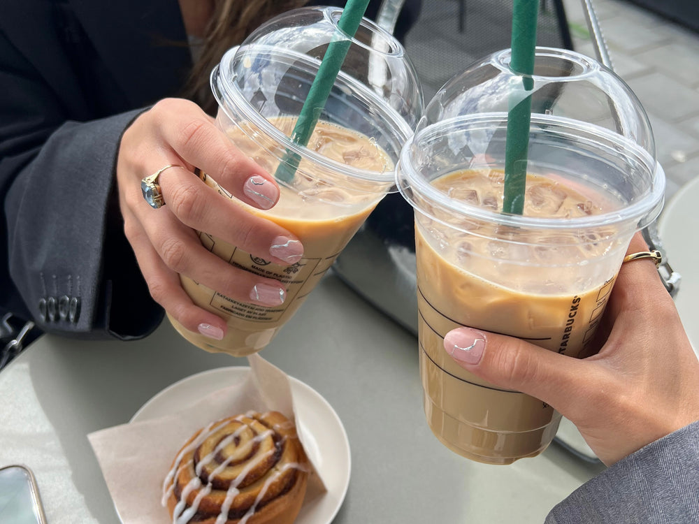 Two coffee cups cheersing with hands that are both wearing a Maniac gel manicure