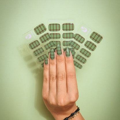 Old Money gel nail sticker sheets by Maniac Nails on a green background, hand with check print nails