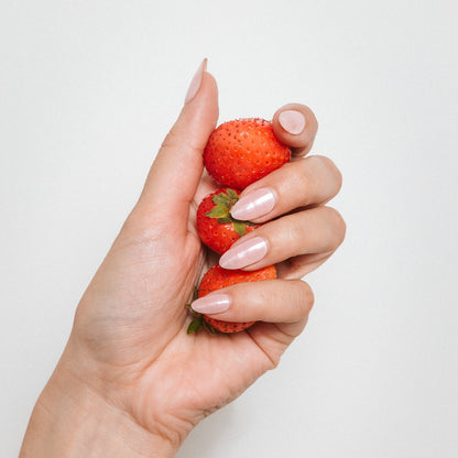 Hand with Strawberry Glaze gel nail stickers by Maniac Nails holding strawberries, milky pink nails