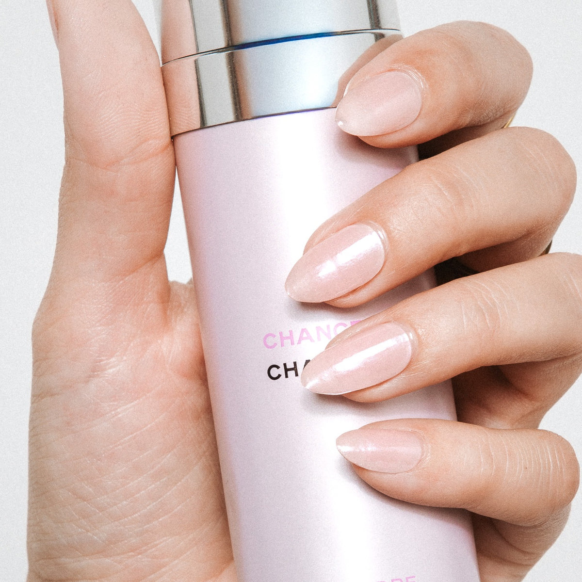 Hand with Strawberry Glaze nail stickers by Maniac Nails holding a pink bottle, glossy pink nails