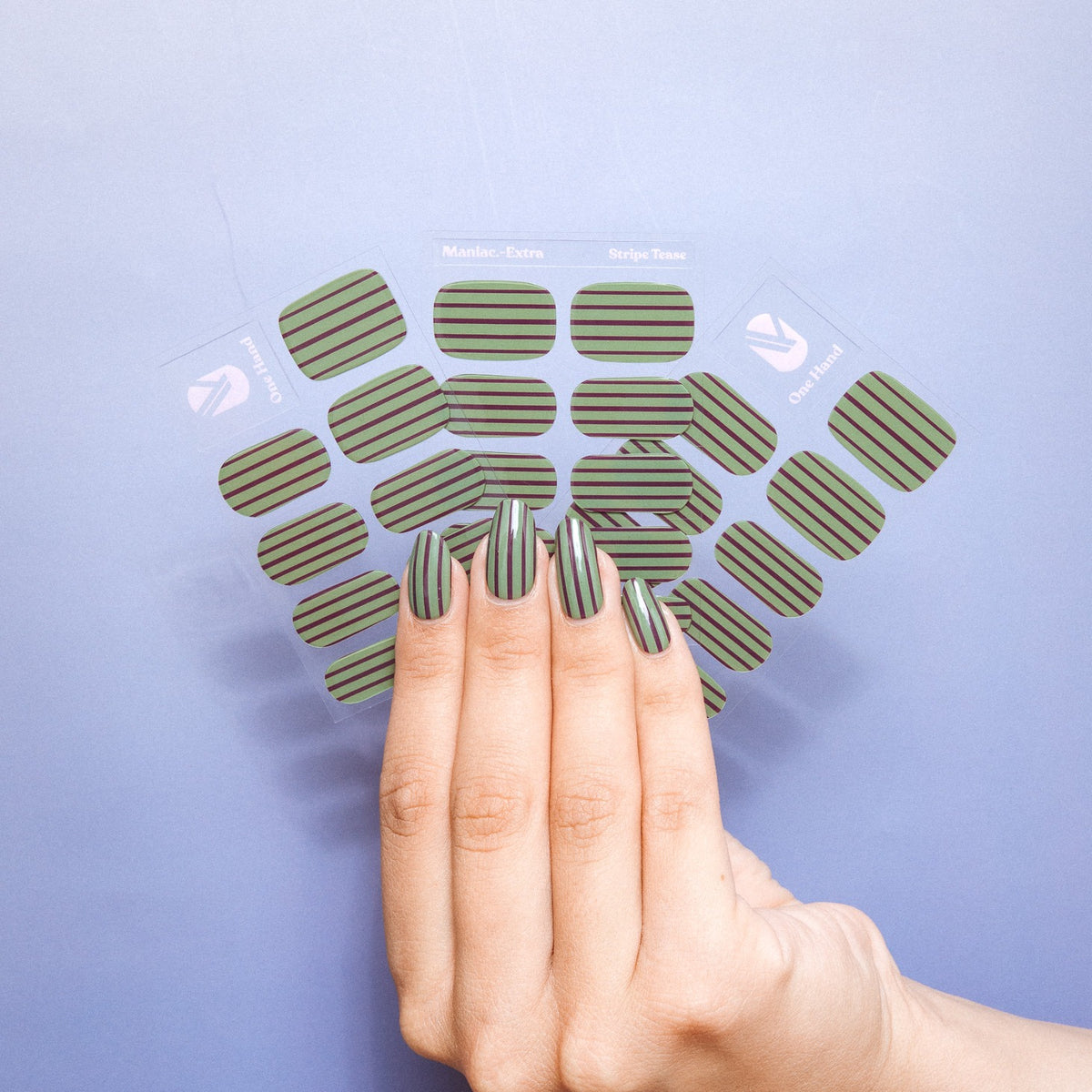 Hand holding Stripe Tease gel nail sticker sheets by Maniac Nails on a lilac background