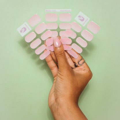 Hands holding Sugar Shimmer gel nail sticker sheets by Maniac Nails on a green background