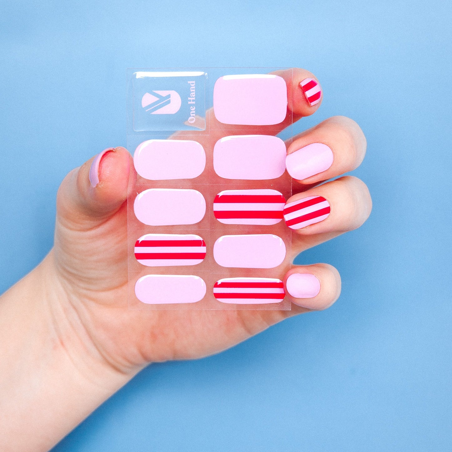Hand holding a Suzy's Candy gel nail sticker sheet by Maniac Nails, pink and red stripes