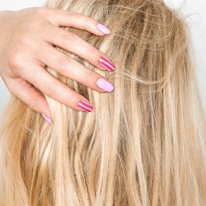 Hand with Suzy's Candy gel nail stickers by Maniac Nails in blonde hair, pink striped nails