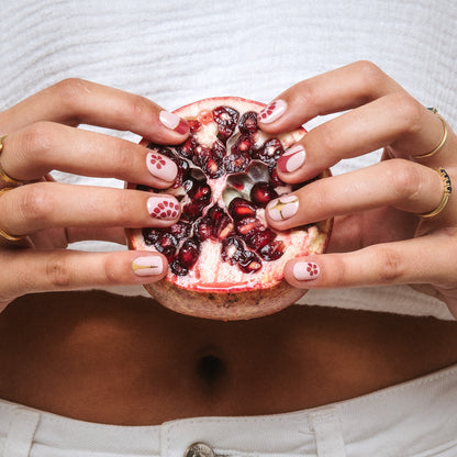 Hands with The Whole Bunch gel nail stickers by Maniac Nails holding a pomegranate, nude nails with red flowers
