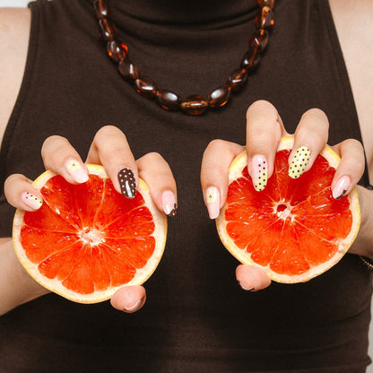 Hands with Toast and Honey gel nail stickers by Maniac Nails holding grapefruit, brown and cream dotted nails