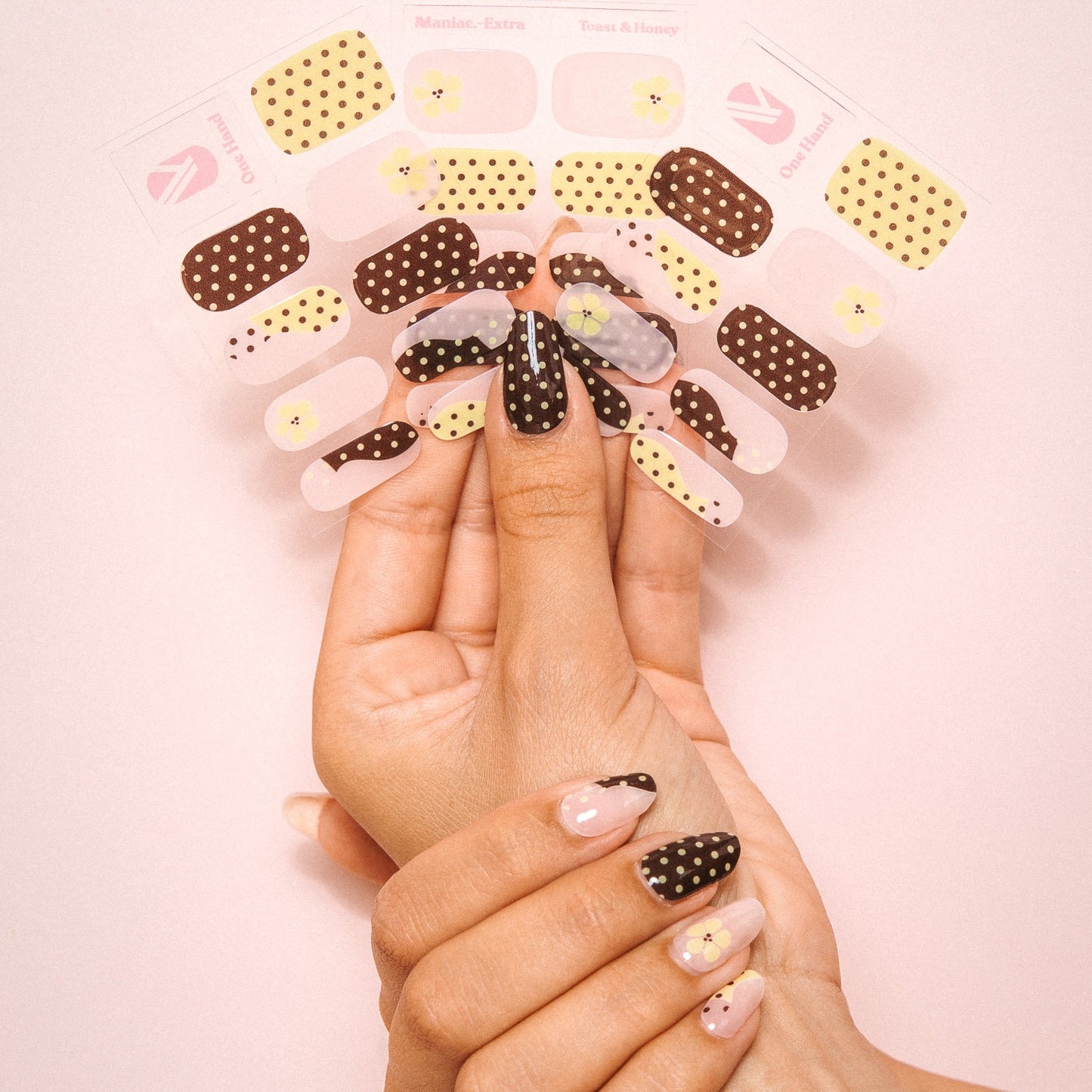 Hands holding Toast and Honey gel nail sticker sheets by Maniac Nails, dotted nail wraps