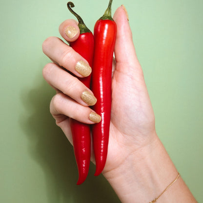 Hand with Unstoppable gold glitter gel nail stickers by Maniac Nails holding red chili peppers