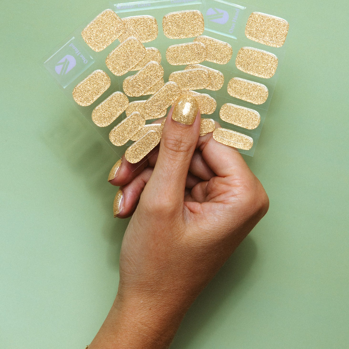 Hand holding Unstoppable gold glitter gel nail sticker sheets by Maniac Nails