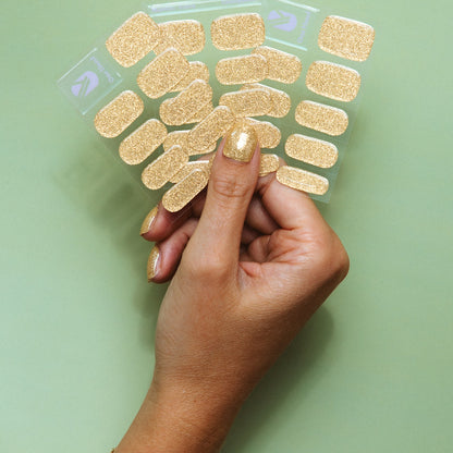 Hand holding Unstoppable gold glitter gel nail sticker sheets by Maniac Nails