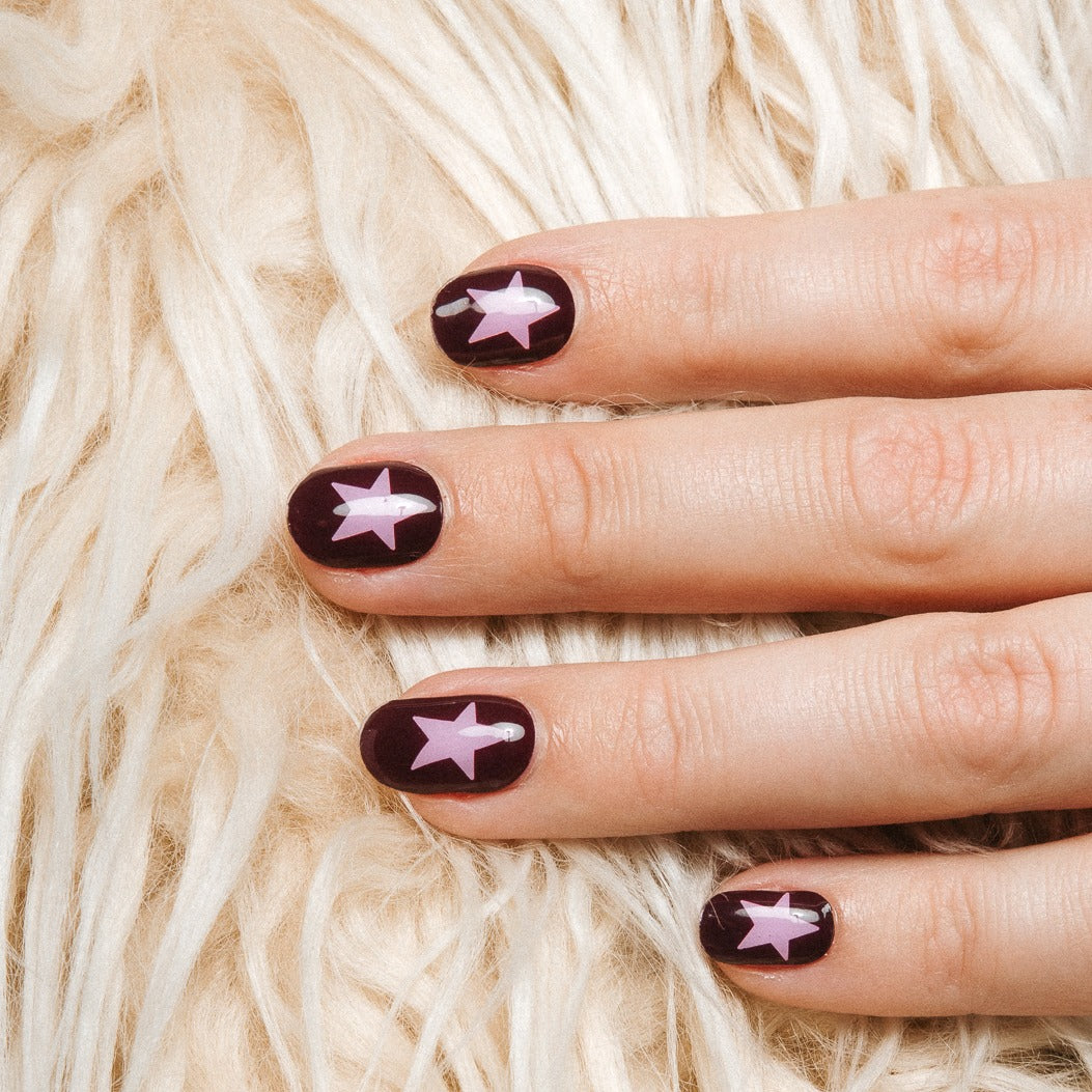 Close-up of Wishing Star gel nail stickers by Maniac Nails, deep plum manicure with pink stars