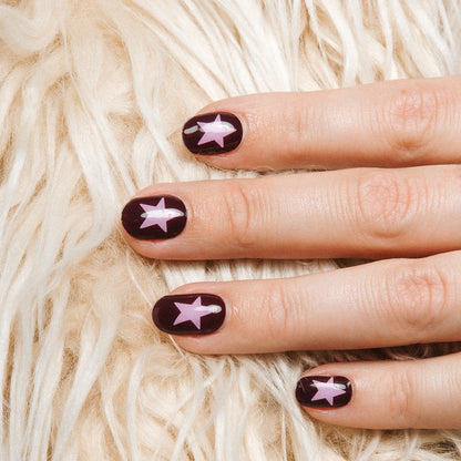 Close-up of Wishing Star gel nail stickers by Maniac Nails, deep plum manicure with pink stars